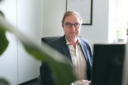 Mann mit Brille sitzend am Computer, lächelt freundlich 